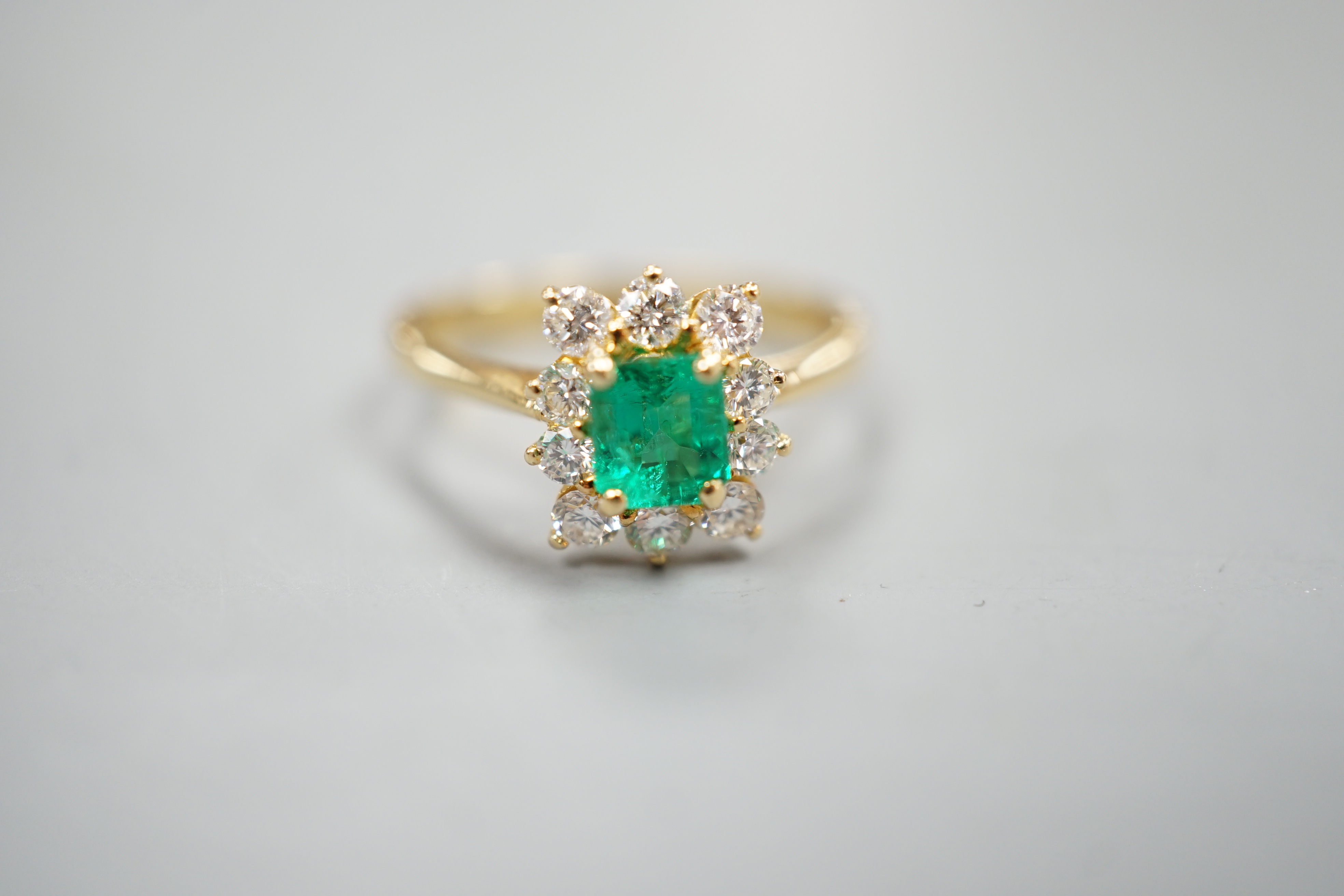 A 750 yellow metal, emerald and diamond set cluster ring, size m, gross weight 3.2 grams.